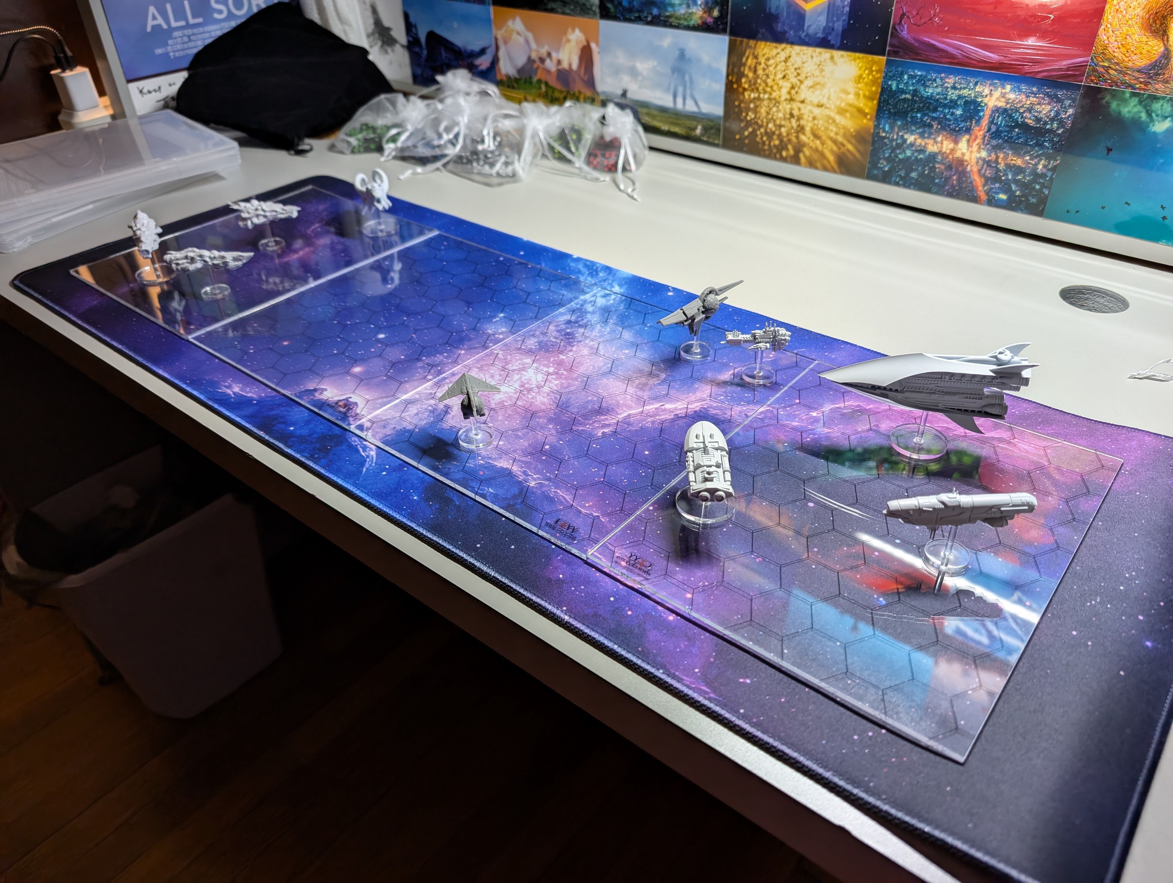 A transparent hex grid with miniatures of space ships on it that is sitting on a neoprene mat depicting outer space.